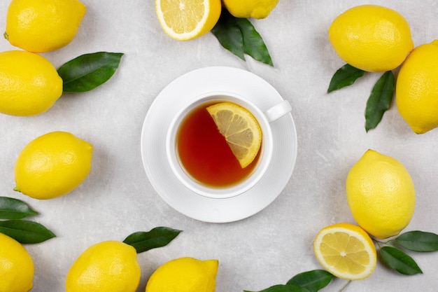 Cup of tea with fresh lemons and leaves on light gray concrete background. Hot healthy beverage. Immune defence, vitamin c. Top view.