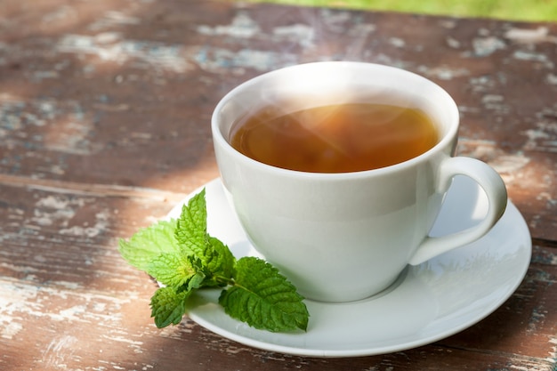 A cup of tea with a green leaf on old wooden board