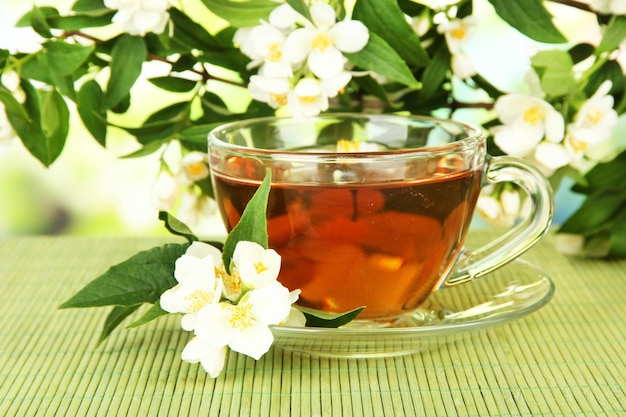 Cup of tea with jasmine on bamboo mat on bright background