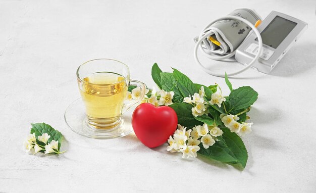 A cup of tea with jusmine flower and blood pressure monitor\
beverage against heart pressure