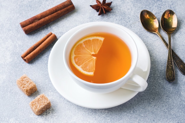 Cup of tea with lemon and brown sugar, cinnamon and anise on the table.