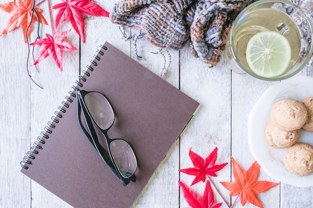 Cup of tea with lemon, cookie, scarf,notebook,glasses and maple leaves on wooden table.