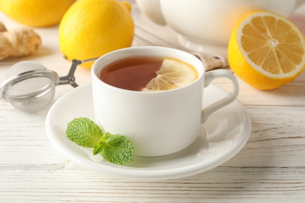 Cup of tea with lemon, mint, strainer, ginger and teapot on wooden, close up