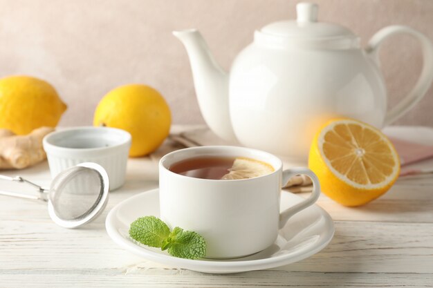 Cup of tea with lemon, mint, strainer, ginger and teapot on wooden, space for text