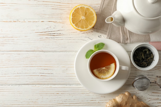 Cup of tea with lemon, mint, strainer, ginger and teapot on wooden, top view