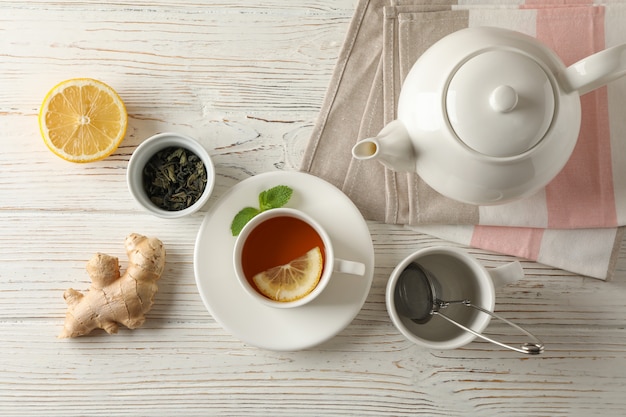 Cup of tea with lemon, mint, strainer, ginger and teapot on wooden, top view