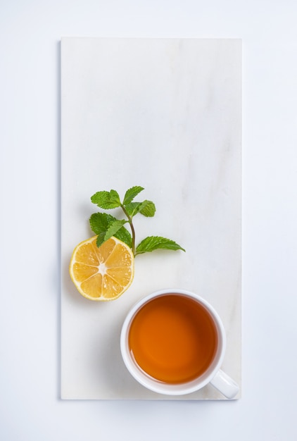 Cup of tea with lemon and mint on  white marble background. Top view and copy space