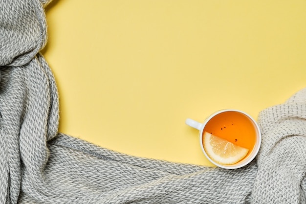 Una tazza di tè con un limone e una sciarpa su uno sfondo giallo.