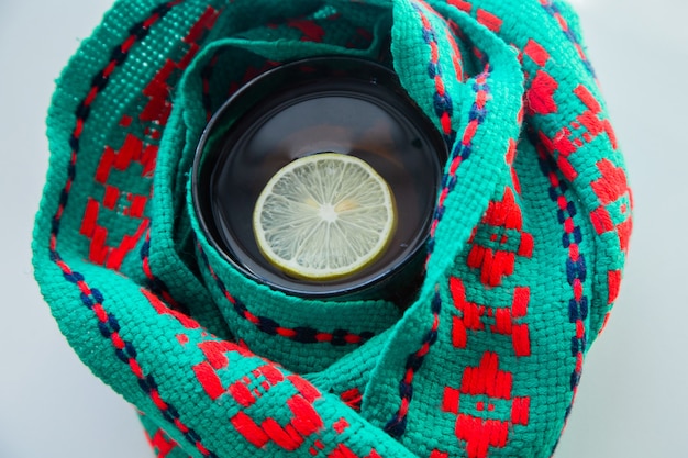 A cup of tea with lemon wrapped in a green and red scarf  high quality photo