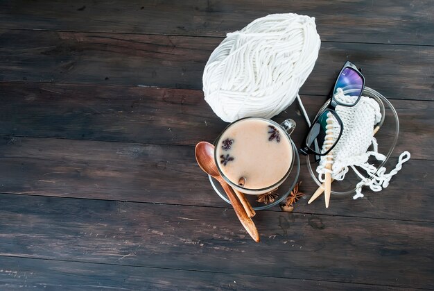 Foto tazza di tè con latte, fili per maglieria e bicchieri su un tavolo di legno.