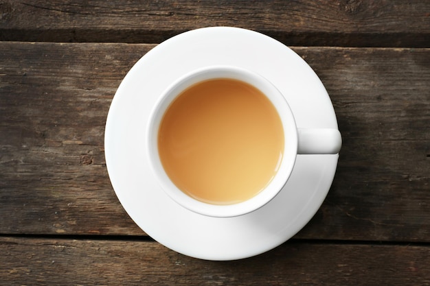 Cup of tea with milk on wooden background top view