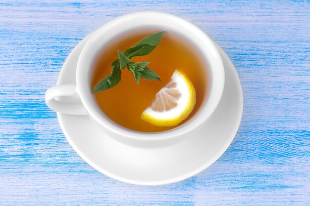 A cup of tea with mint and lemon on a blue wooden background