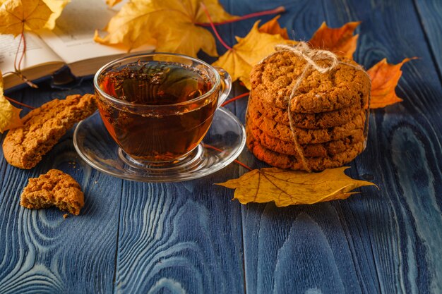 Cup of tea with old book, autumn leaves on wooden table