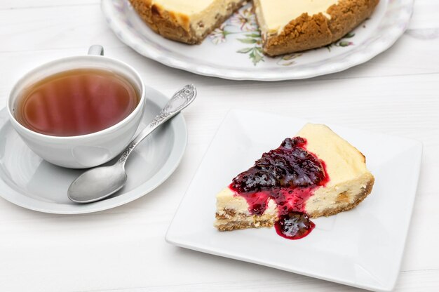 Cup of tea with piece of cheesecake with jam on the table