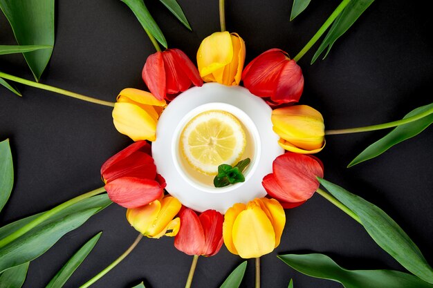 Cup of tea with red and yellow tulip around.