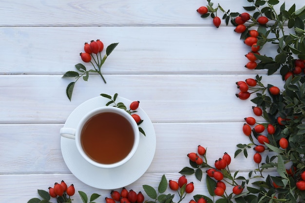 白い木製の背景にバラの果実と紅茶のカップ