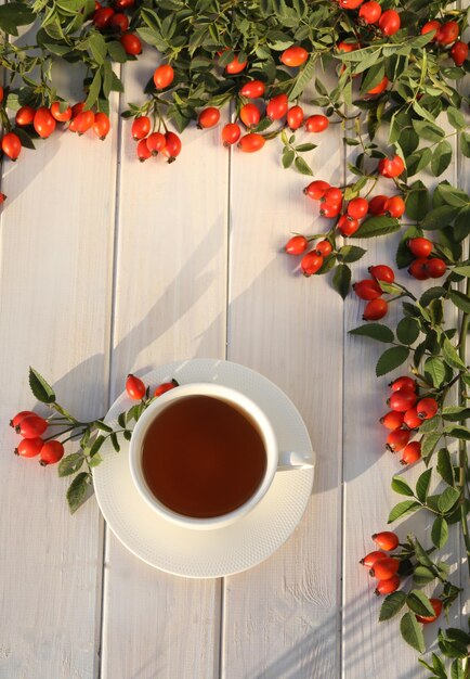 Cup of tea with rose berries on a white wooden background