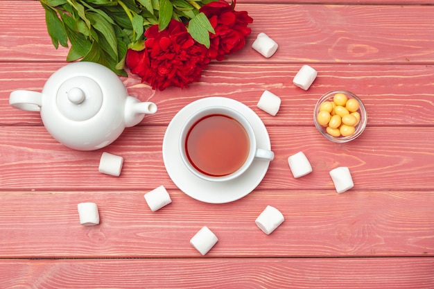 Cup of tea with sweets and flowers on wooden table