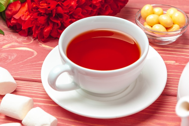 Cup of tea with sweets and flowers on wooden table