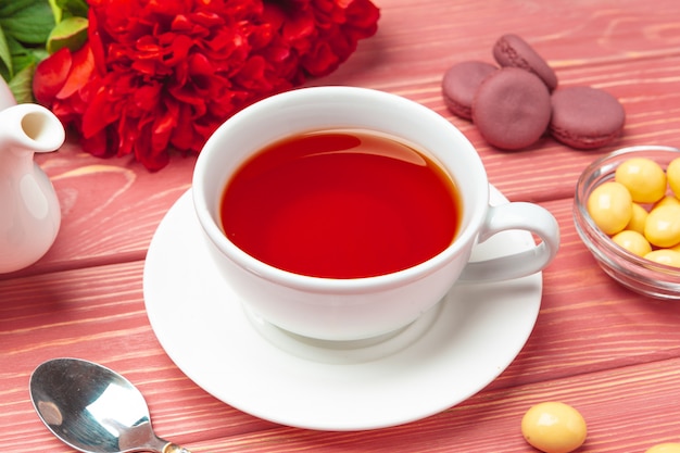 Cup of tea with sweets and flowers on wooden table