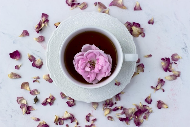 A cup of tea with a tea rose on a white marble background good\
morning top view