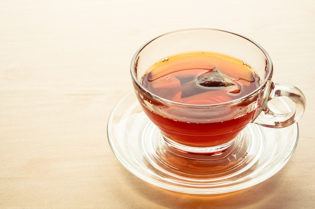 A cup of tea on the wooden table, tea bag in glass.