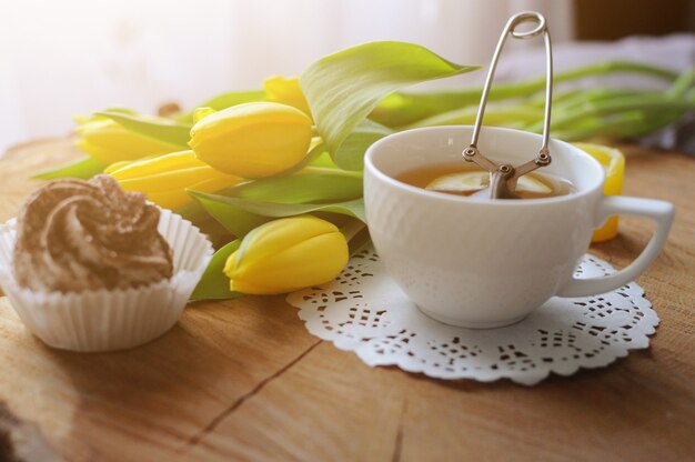 A cup of tea on wooden table with marshmallow and yellow tulips. Breakfast in bed