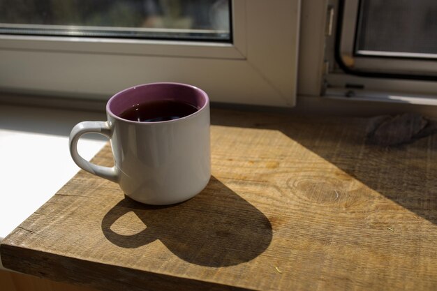 A cup of tea on a wooden tray is standing by the window