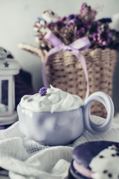 A cup of whipped cream sits on a white tablecloth with a purple ribbon.