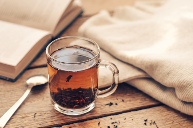 Чашка с черным заваренным чаем на деревянном столе с книгой и теплым свитером