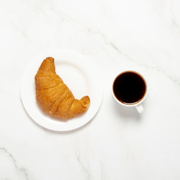 Cup with black coffee and croissant on a marble background