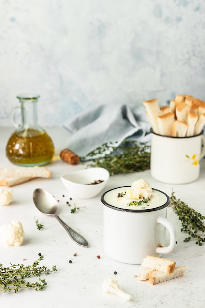 Cup with cauliflower cream soup garnish with fresh cauliflower, thyme and bread. Autumn or winter comfort food. Healthy dinner.