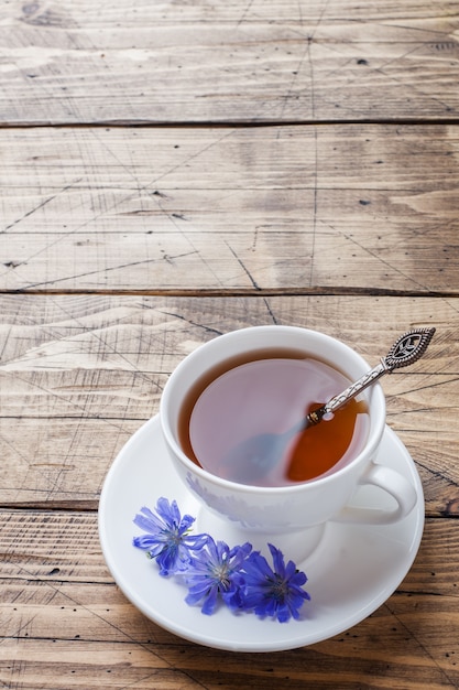 チコリの飲み物と木製のテーブルの上の青いチコリの花のカップ