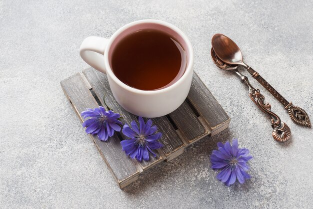Чашка с напитком цикория и синих цветов цикория на сером столе