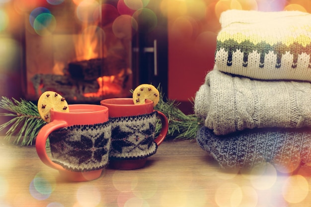 Foto tazza con ornamento di natale vicino al camino tazza in guanto lavorato a maglia rosso in piedi vicino al caminetto