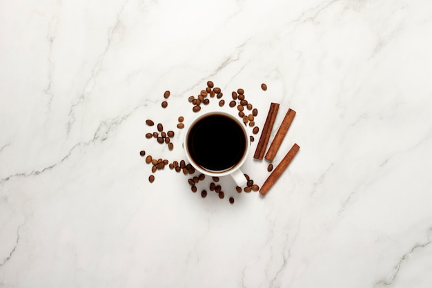 Cup with coffee, cinnamon sticks and coffee beans on a marble table. Flat lay, top view