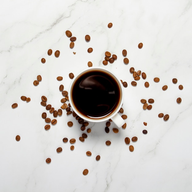 Cup with coffee and coffee grains on a marble table. Square. Concept breakfast, black coffee, coffee for the night, insomnia. Flat lay, top view