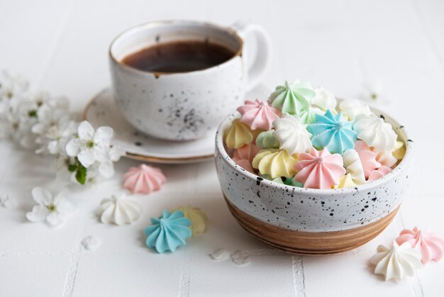 Cup with coffee and small meringues in the bowl  on a tiled surface