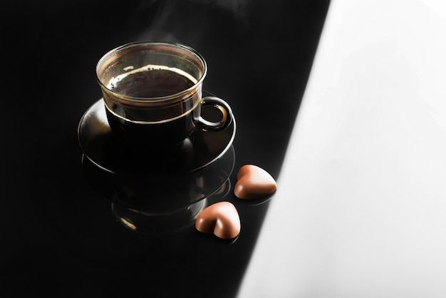 чашка с кофе и паром на черно-белом фоне с конфетами в форме сердца