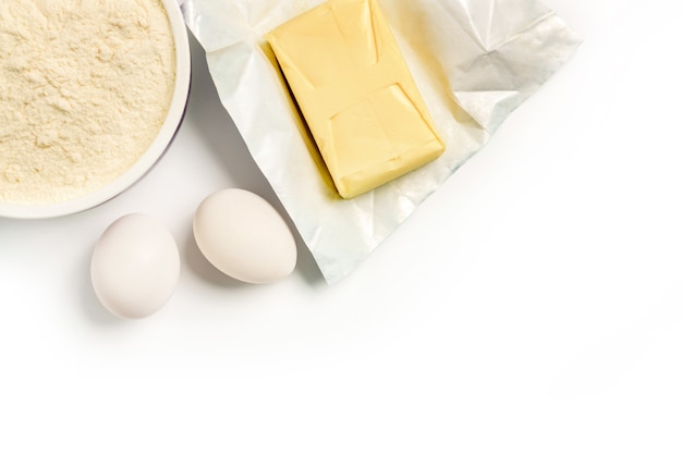 小麦粉、卵、バターと白い背景で隔離のカップ。コピースペースで焼くための材料。