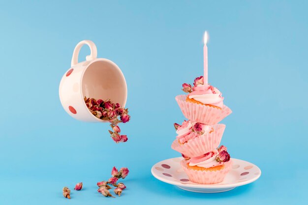 Cup with flowers of rose and three birthday berry muffins on top of each other in pink wrappers