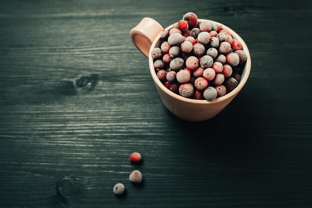 Cup with fresh frozen cranberries on dark rustic background toned image