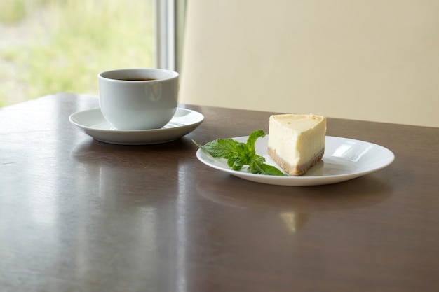Чашка со свежесваренным кофе и ломтик чизкейка на столе в кафе.