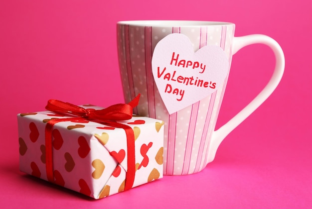 Cup with greeting card and gift box for valentines day on pink background