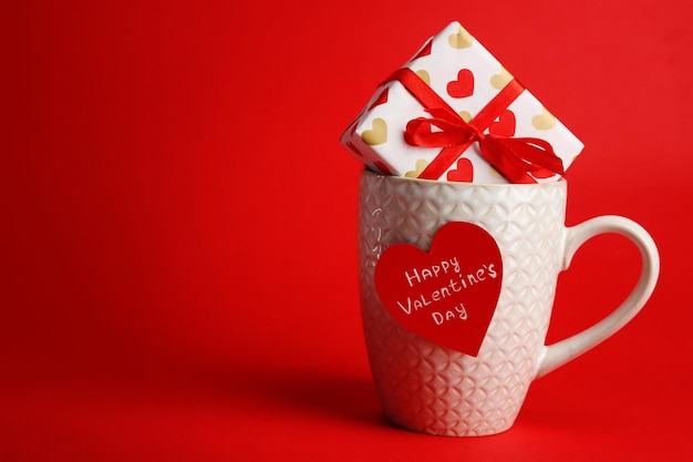 Cup with greeting card and gift box for Valentines Day on red background