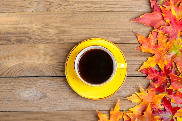 cup with hot black coffee on a wooden table with autumn fallen yellow, orange and red leaves 