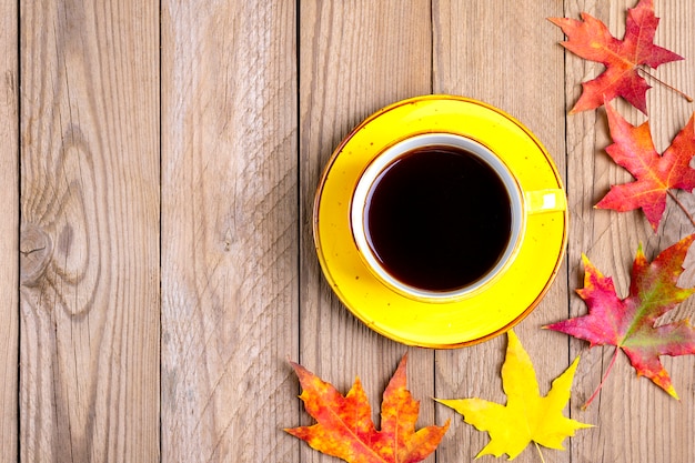 cup with hot black coffee on a wooden table with autumn fallen yellow, orange and red leaves 