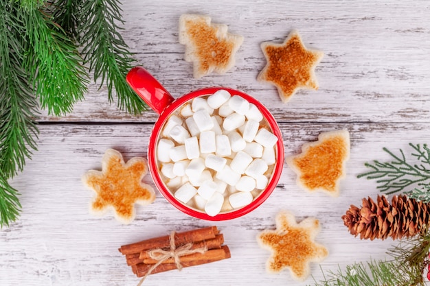 Cup with hot cocoa and marshmallows, toasted shaped bread slices on wooden table