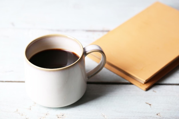 Cup with hot coffee and old book on wooden background