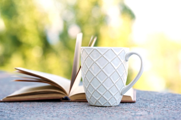 Cup with hot drink and book outdoors